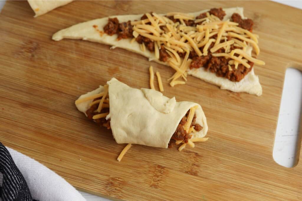 rolling up a crescent roll with sloppy joe filling and cheddar cheese
