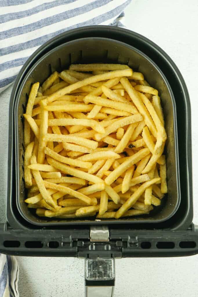 Air fryer frozen french fries in an air fryer basket..jpg