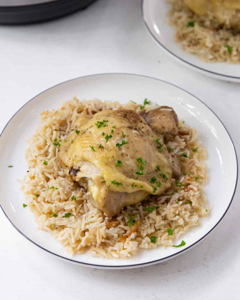 Instant pot chicken thighs on top. of basmati rice on a white plate.