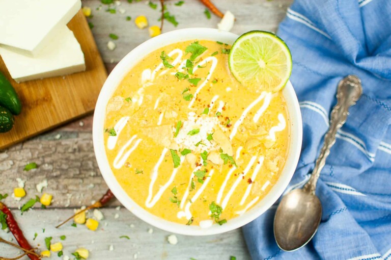 Overhead shot of Corn Soup in a white bowl with a slice of lime and sour cream drizzled on top.