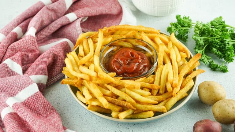 Plate of French fries with small glass bowl of ketchup in the center.