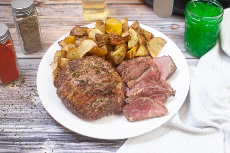 Lamb roast sliced served with potatoes on a white plate.