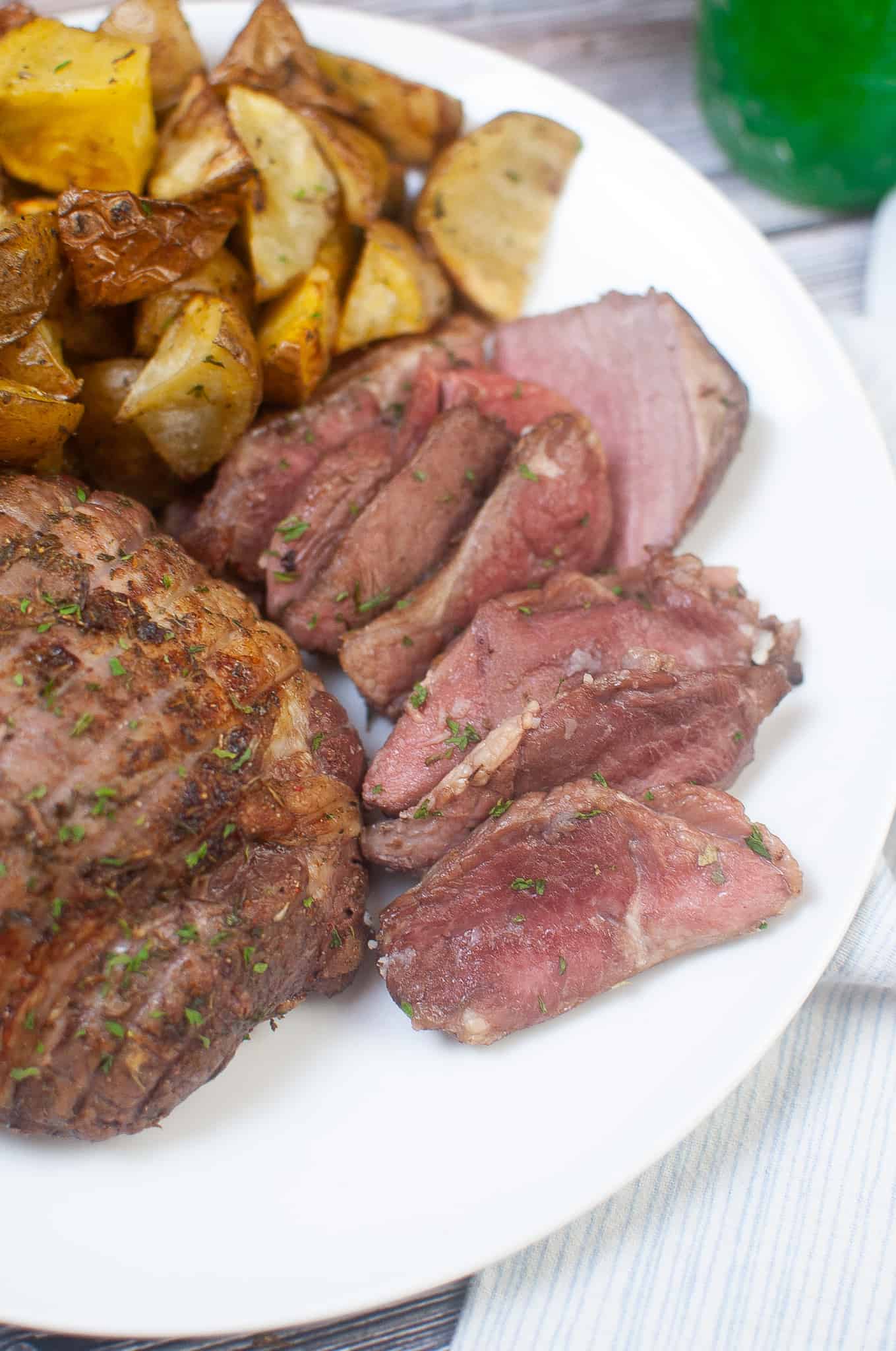 Closeup of sliced lamb on a white plate with diced potatoes.