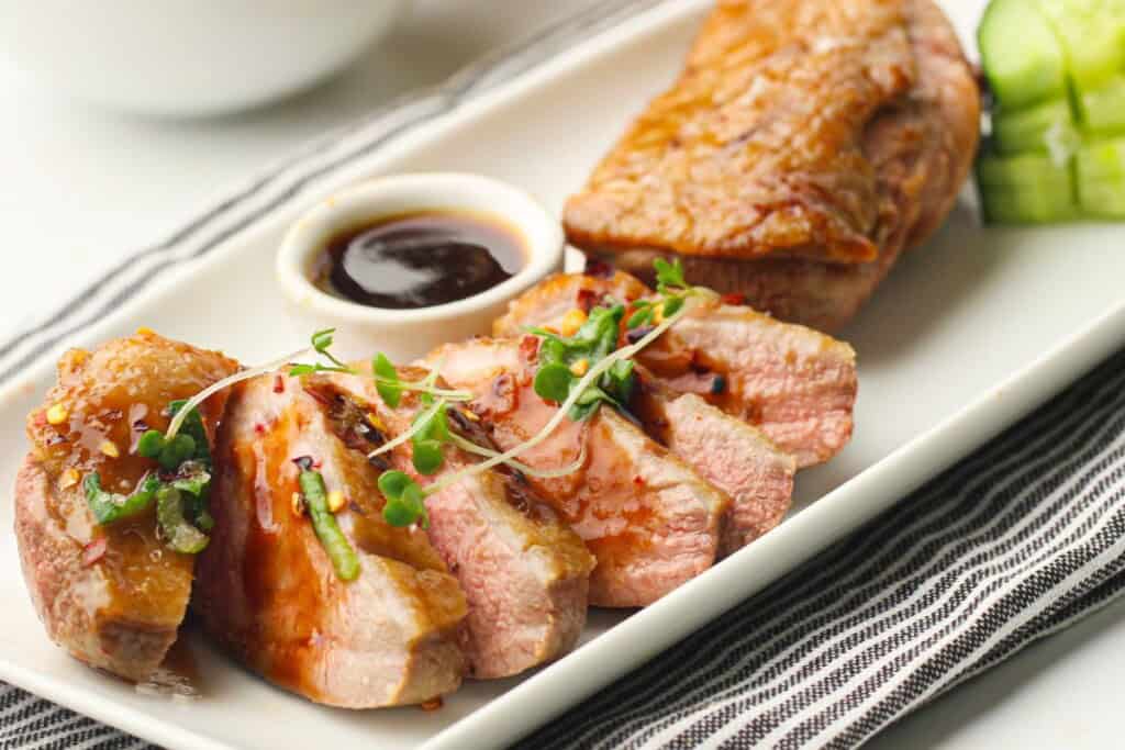 Crispy air fryer duck breast with crackling skin sliced on a plate with plum sauce on the side.