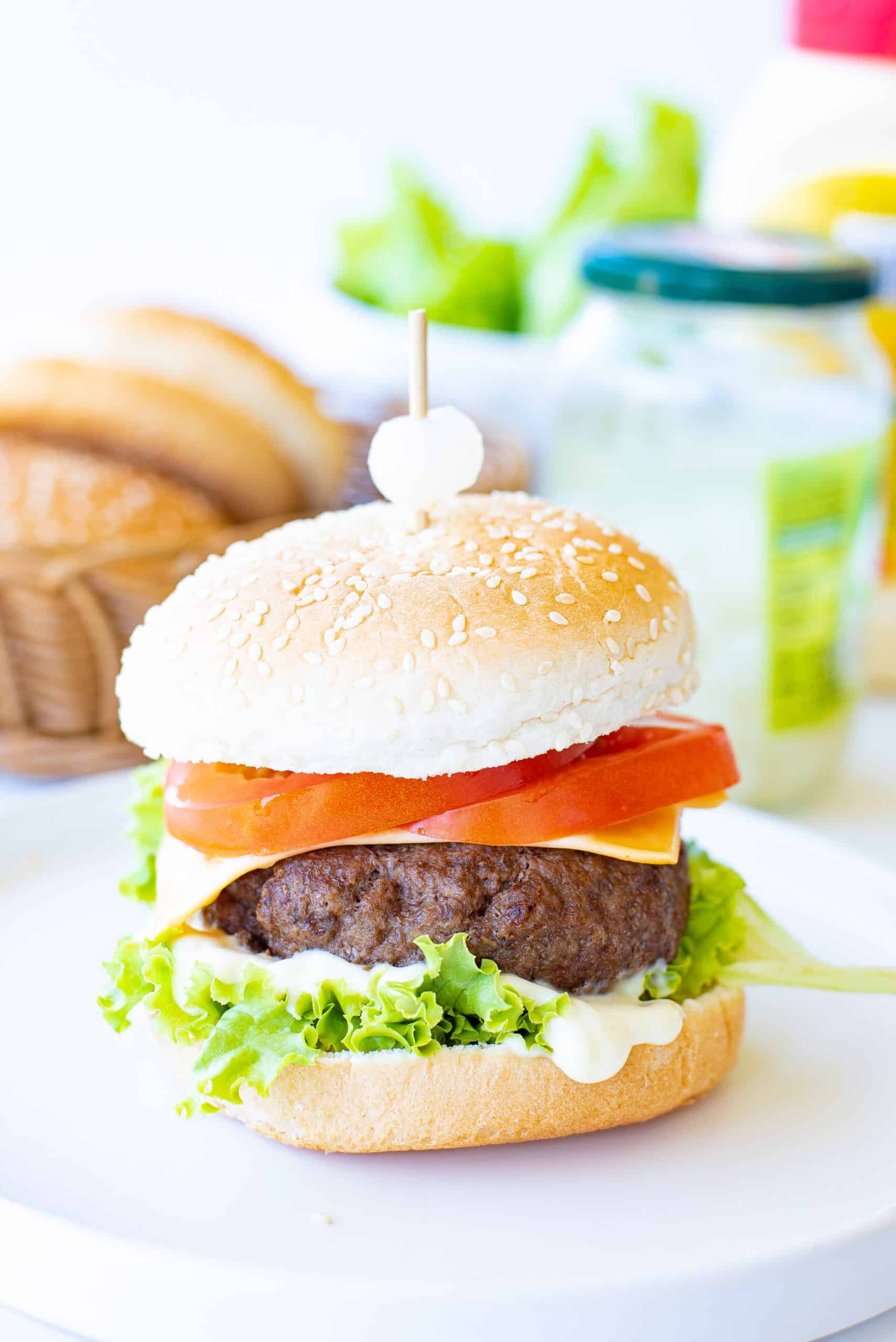 Headon view of hamburger with slice of tomato, cheese, mayonnaise and lettuce.