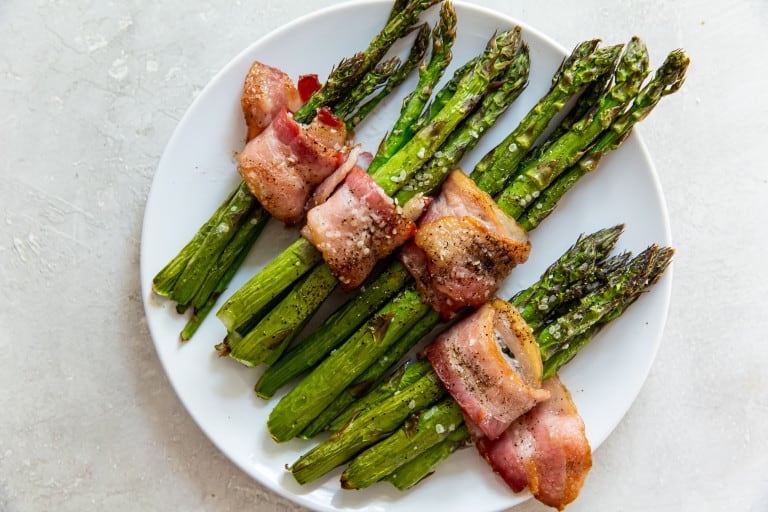 Bacon asparagus with sea salt on a white plate with an overhead view.