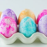 6 Easter eggs dyed different colors with rice in a ceramic carton.