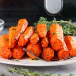 Air fryer roasted carrots on a plate with a fork in front of the air fryer.