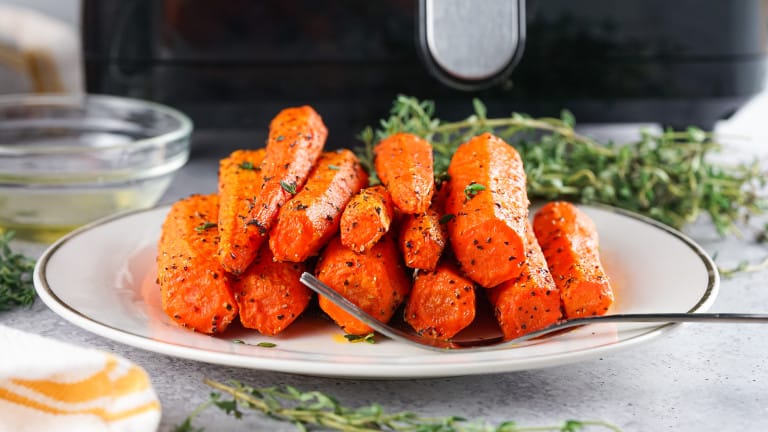 Air fryer roasted carrots on a plate with a fork in front of the air fryer.
