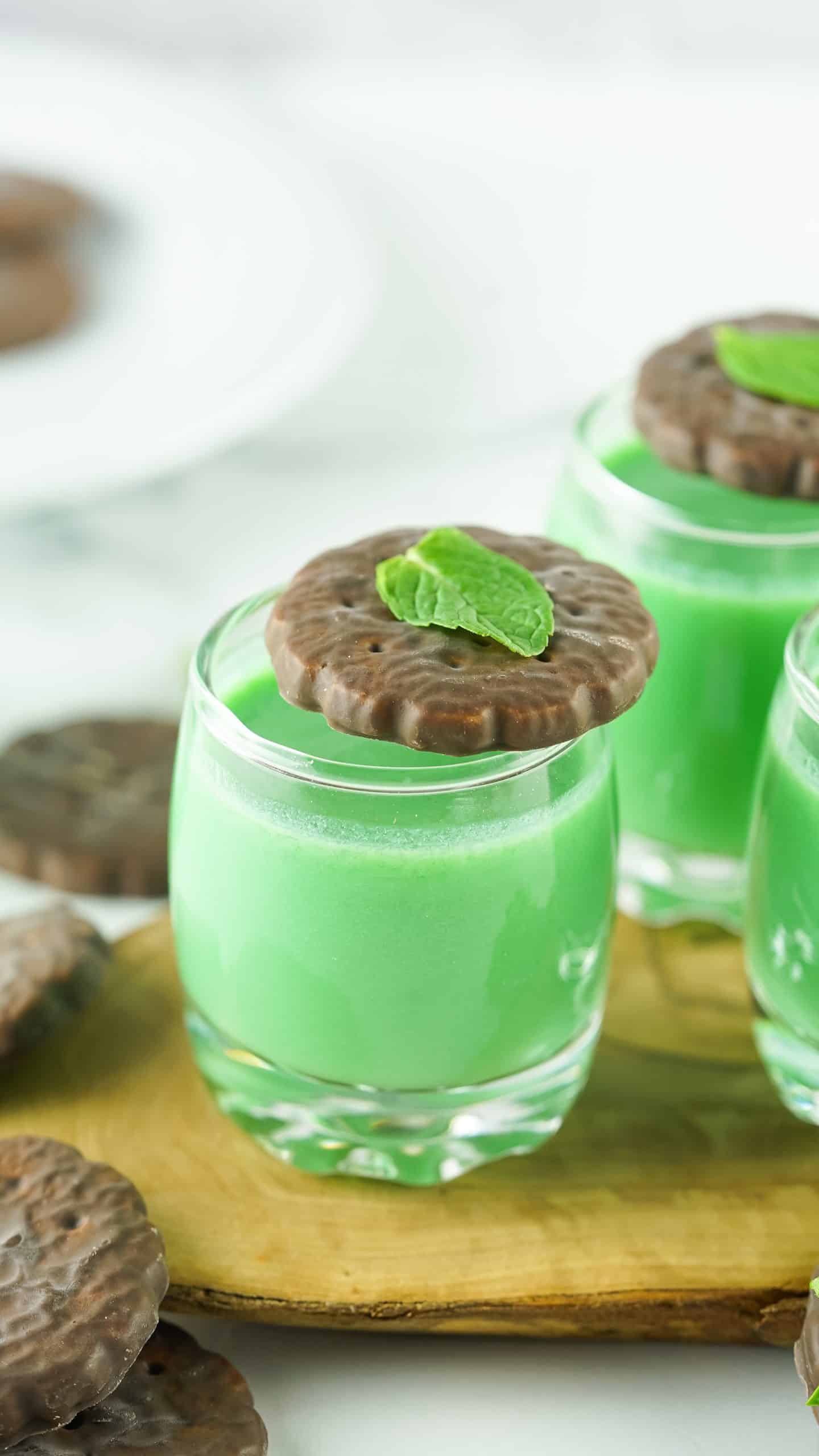 Green shots with chocolate mint cookie and mint leaf on top of it.