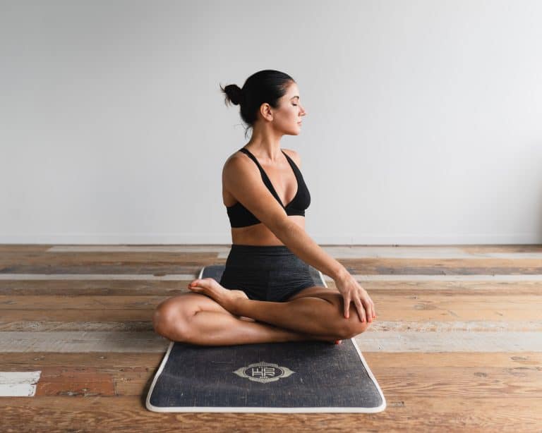 Woman on a yoga mat doing a twist to the side while sitting with legs crossed.