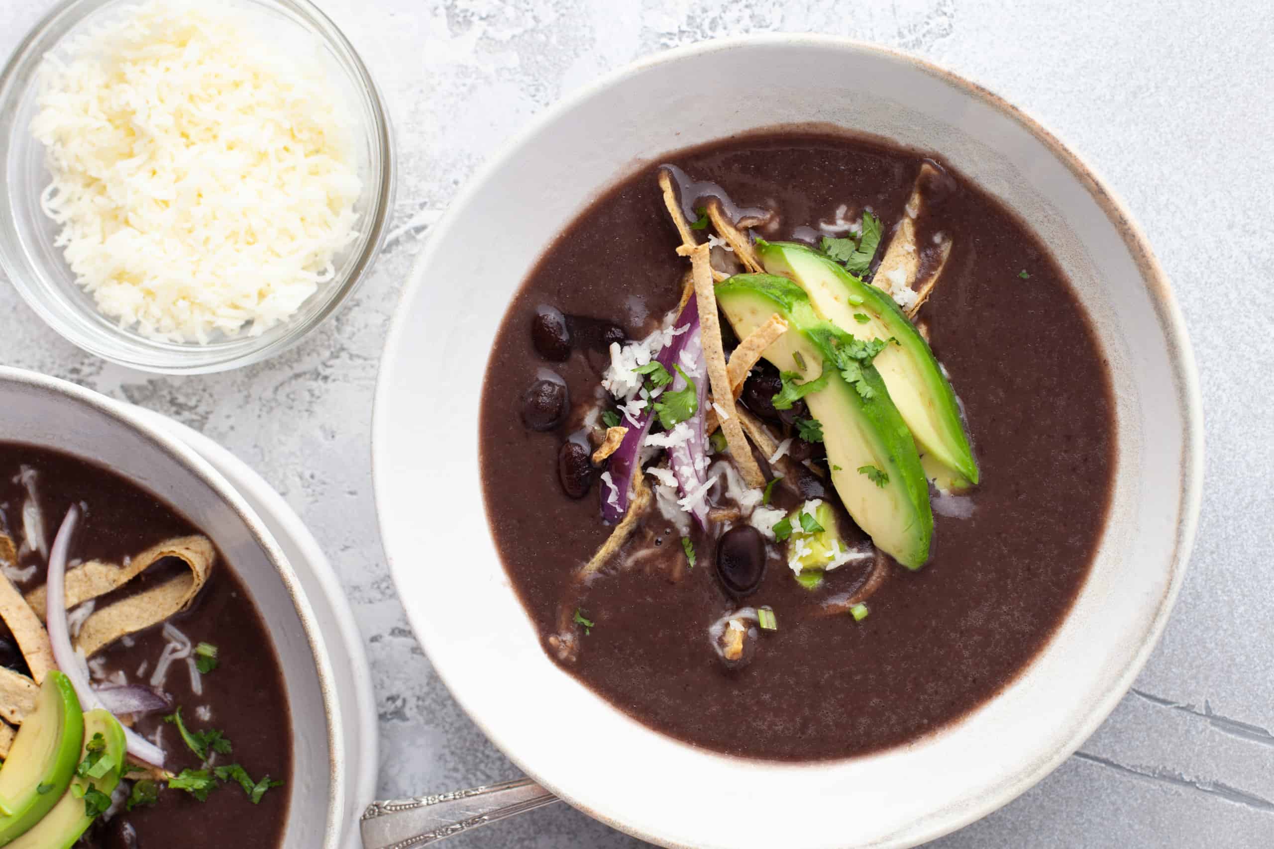 Overhead view of black bean soup with avocado, tortilla strips & red onion slices.