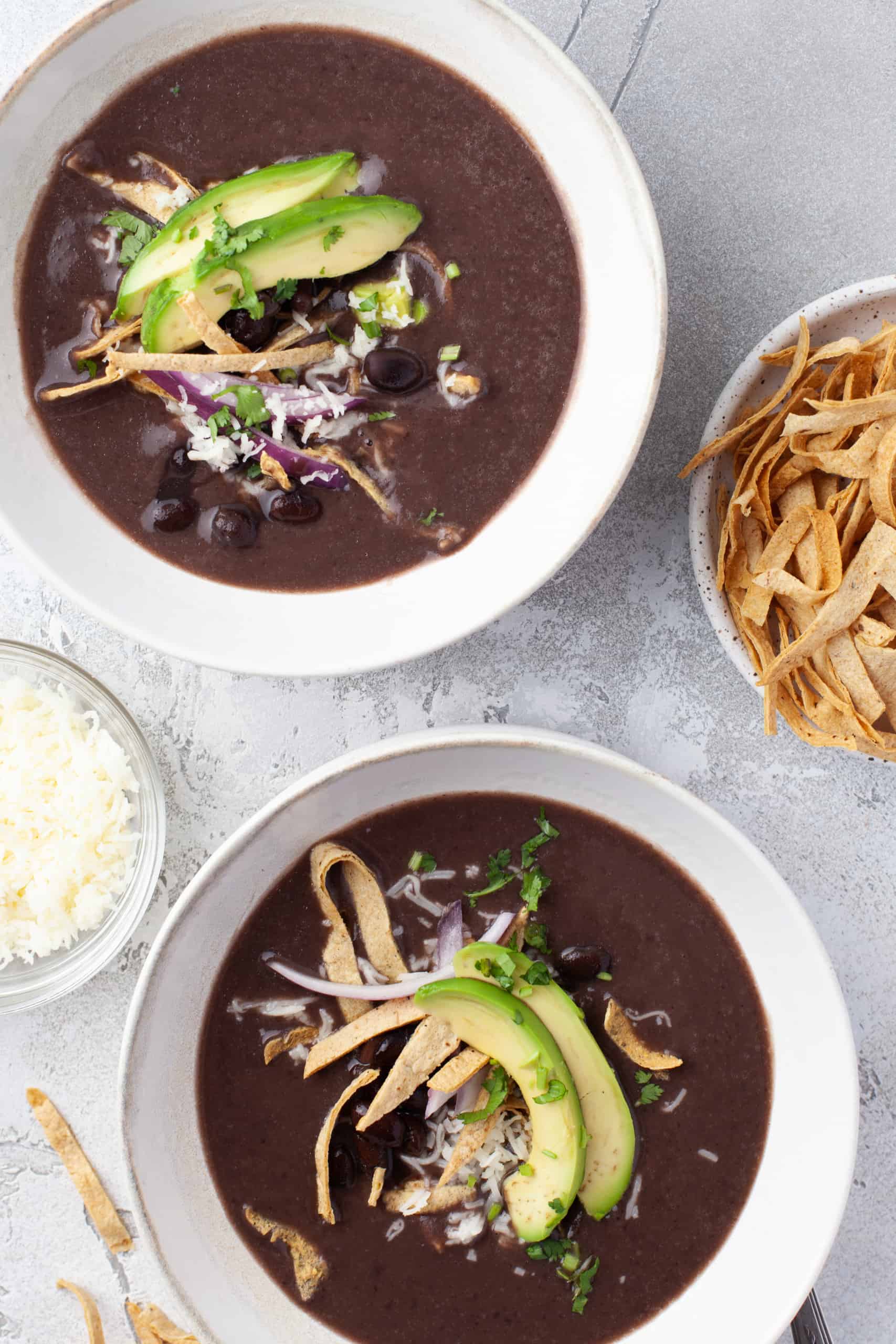 Overhead view of black bean soup with tortilla strips and avocado slices.