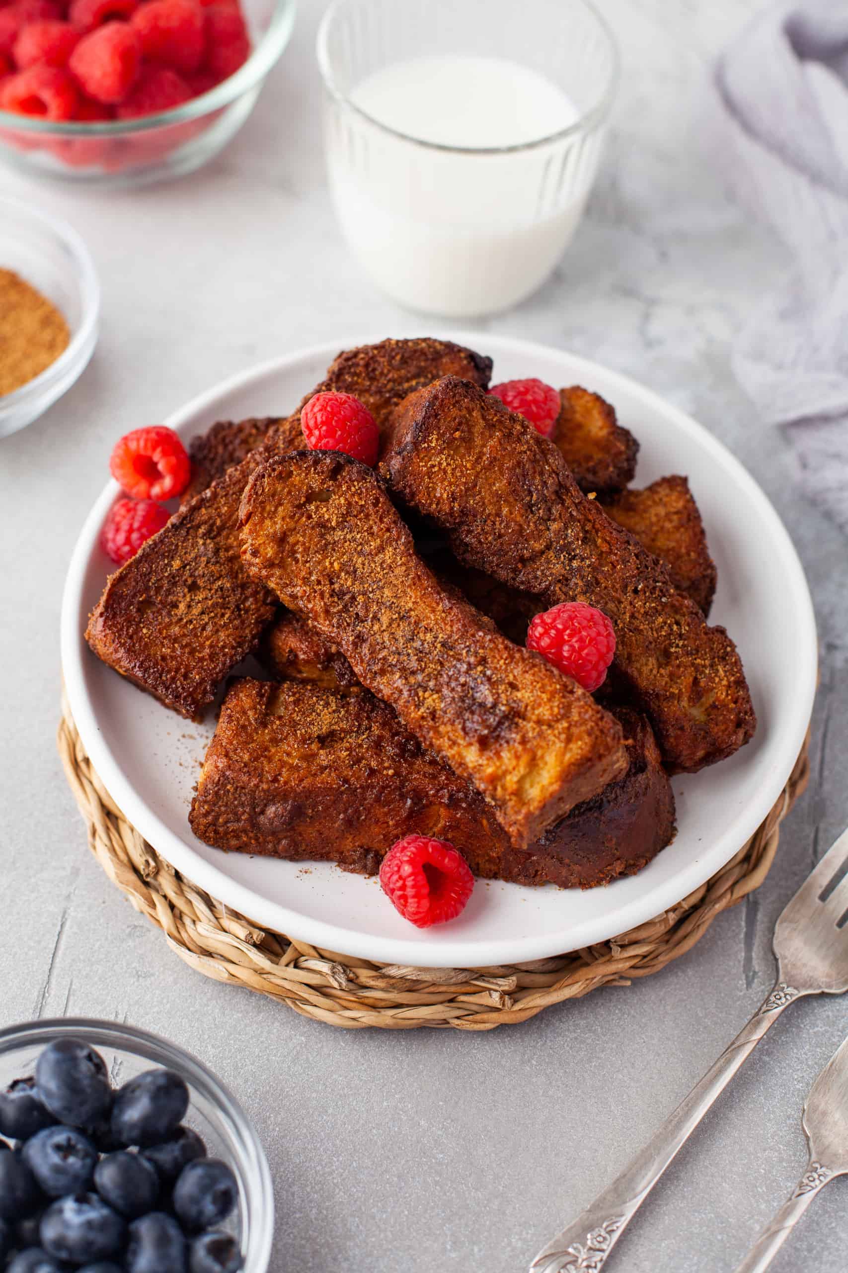 French toast sticks with fresh raspberries on a white plate.