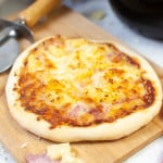 Ham and pineapple pizza on a cutting board.