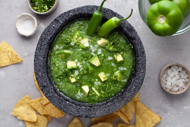 Overhead view of salsa verde with avocado chunks and 2 whole Serrano peppers garnishing it.