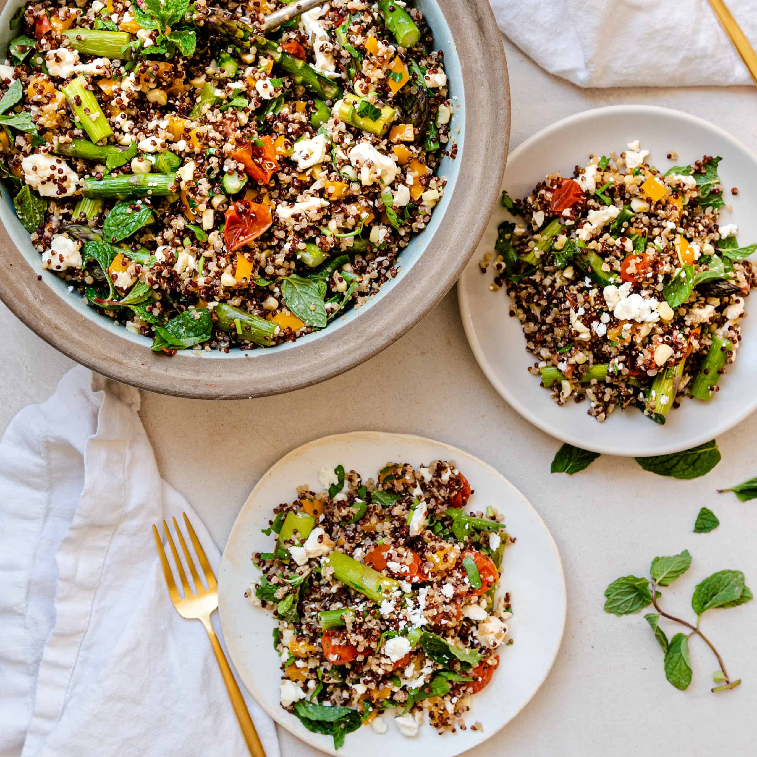 Overhead view of bowl of quinoa salad with roasted vegetables. Two servings of the salad on plates beside the bowl.