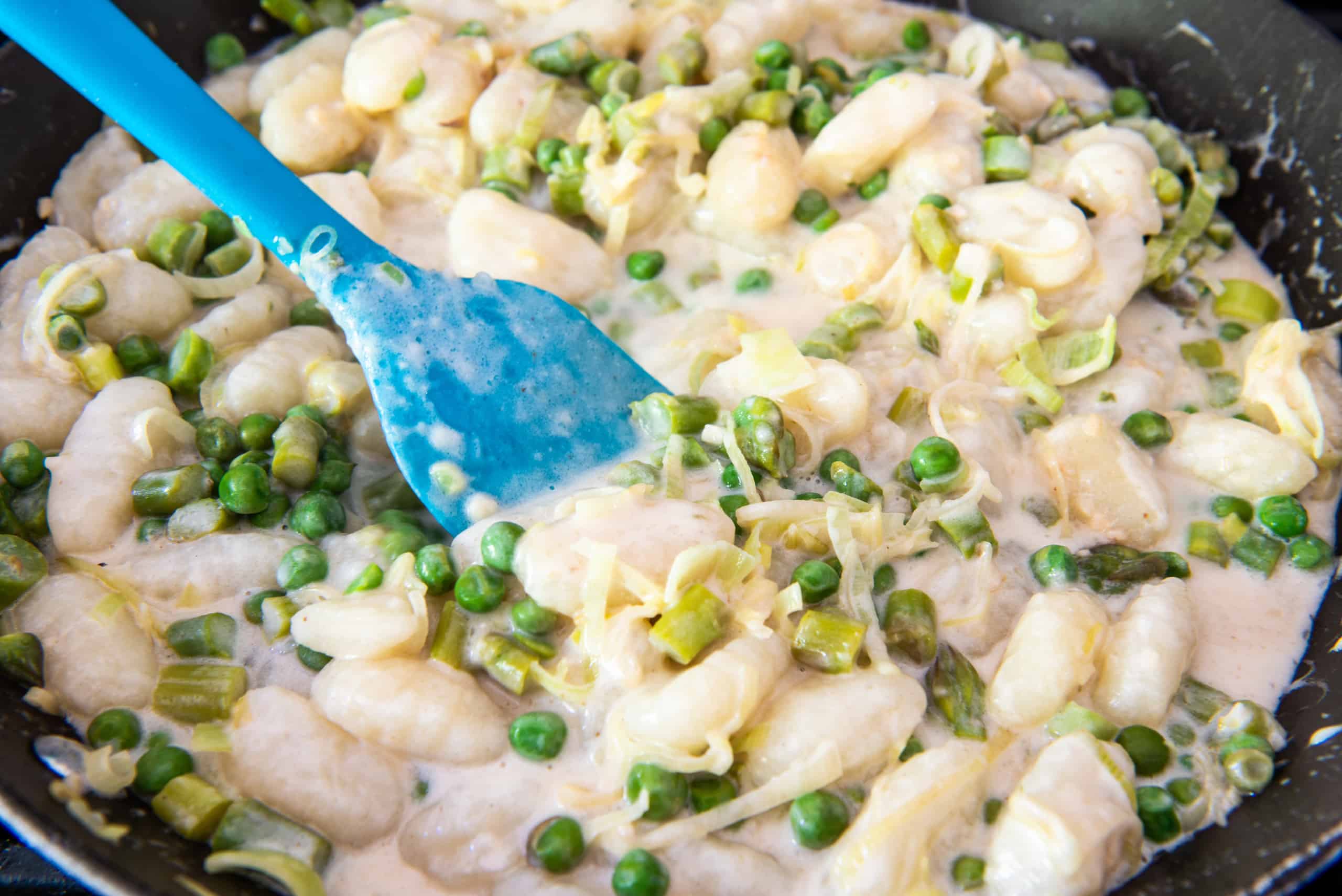 Cheesy gnocchi in a skillet with a blue serving spoon mixing it.