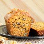 Sliced pumpkin banana bread with walnuts on a black plate.