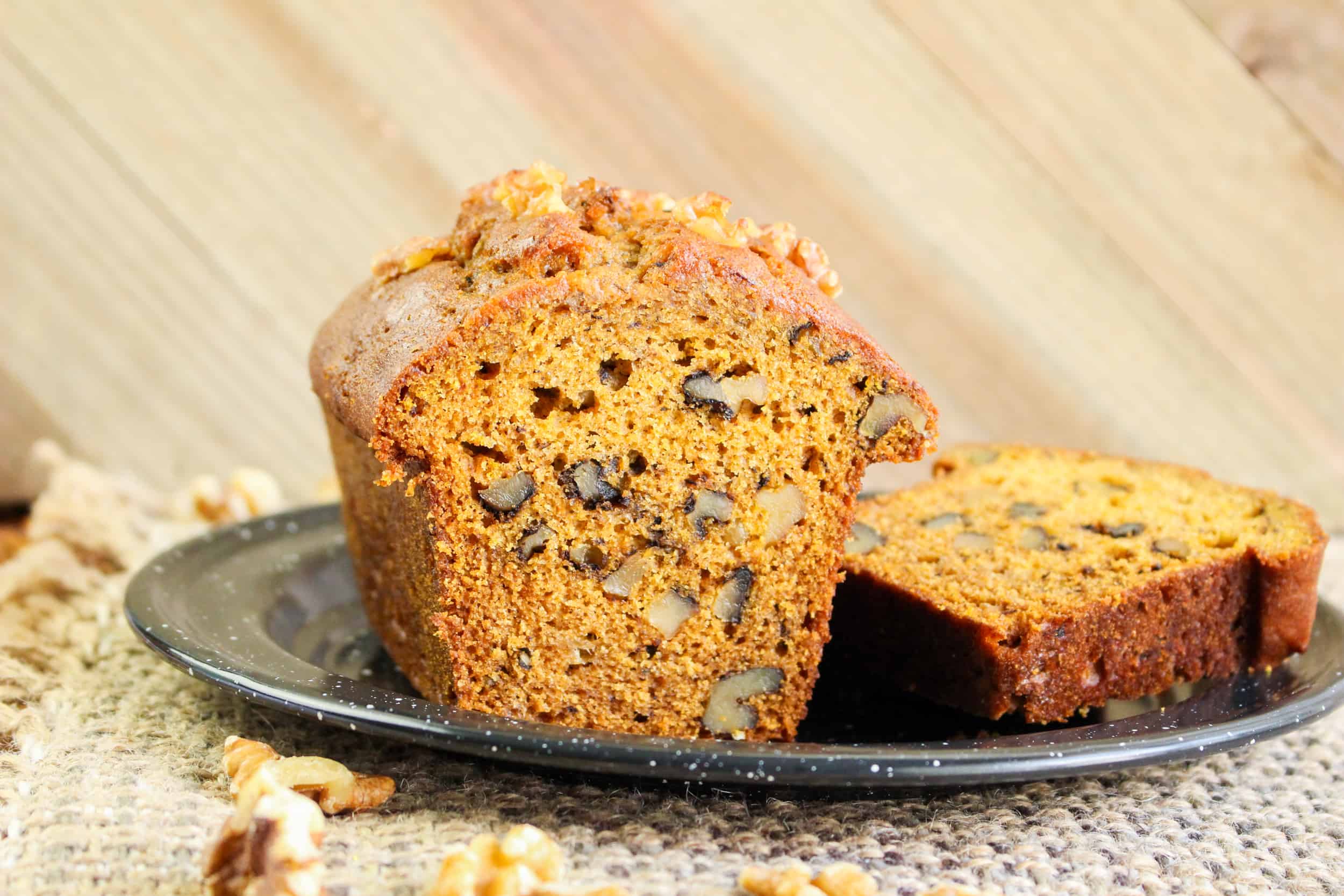 Sliced pumpkin banana bread with walnuts on a black plate.