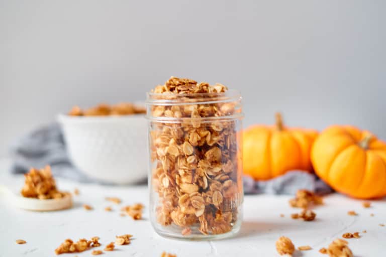 Pumpkin spice granola in a Mason jar with mini pumpkins and a bowlof granola behind it.