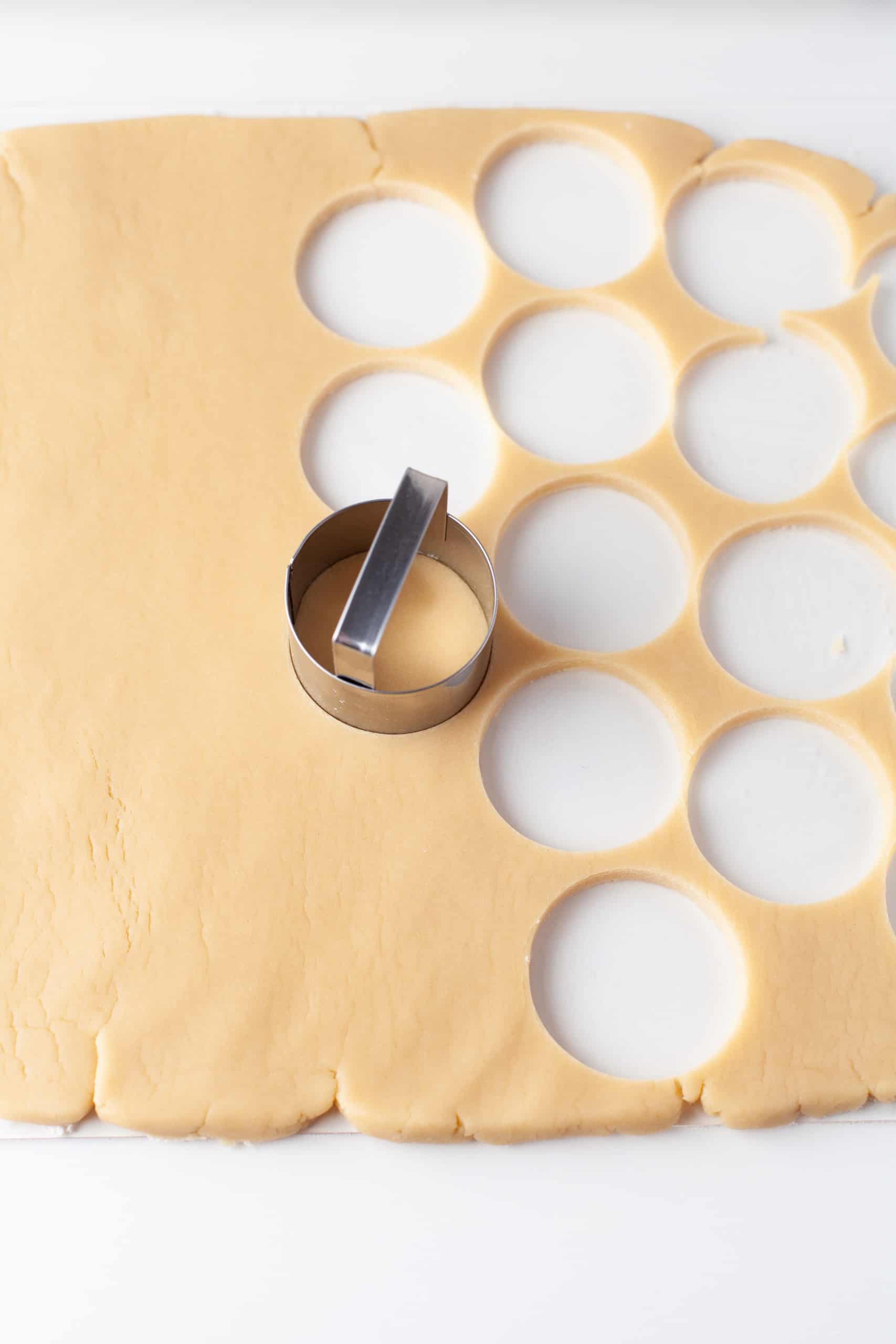 Cutting out cookie dough into circles with a round cookie cutter.