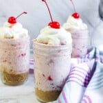 3 Jars of Millionaire Pie with whipped cream and cherries on top.