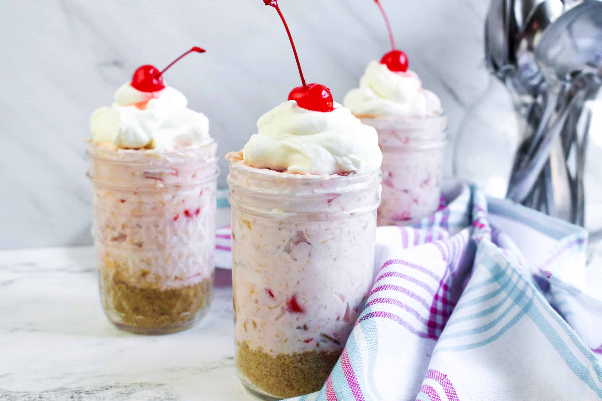 3 Jars of Millionaire Pie with whipped cream and cherries on top.