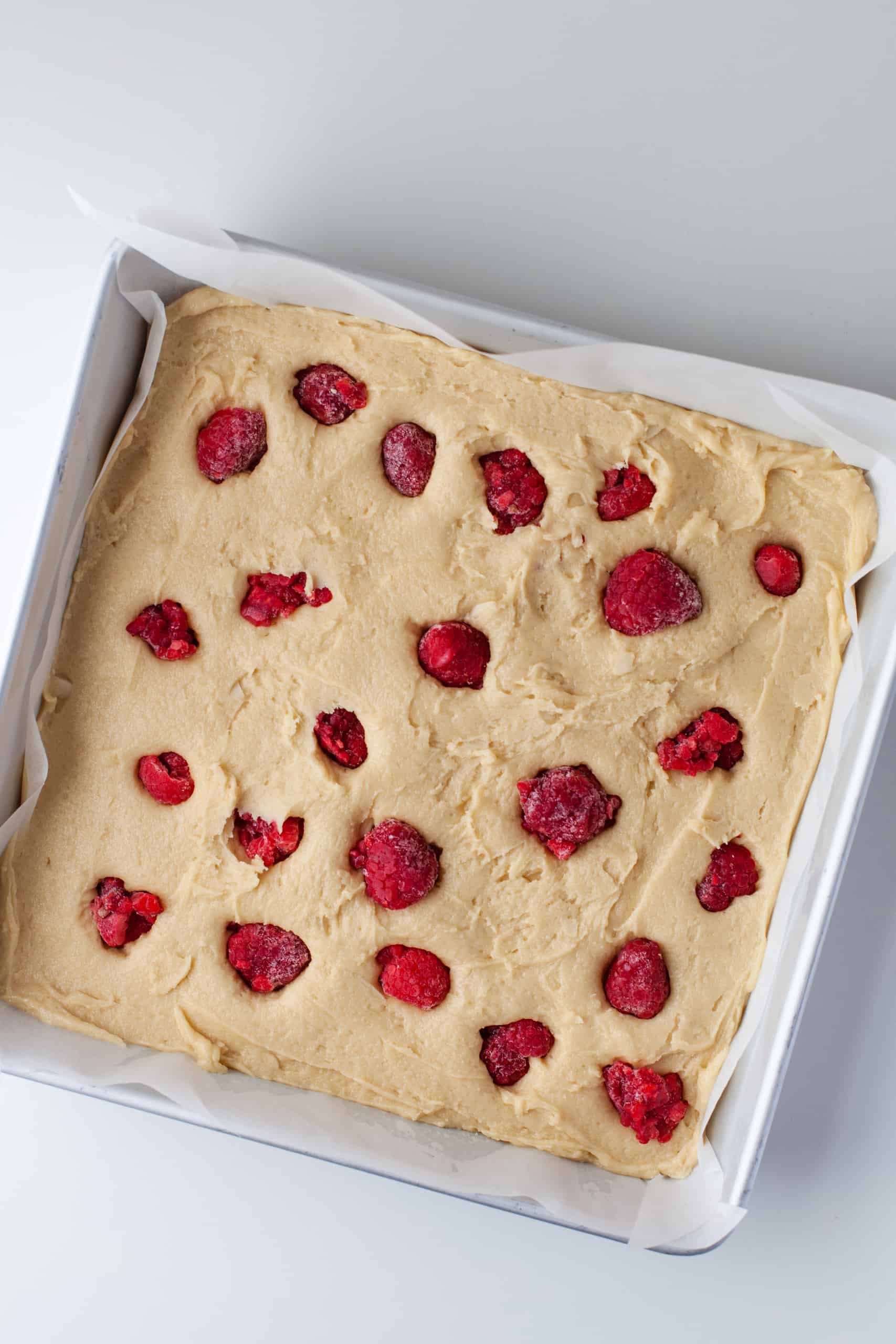 Overhead view of blondie batter with raspberries in a baking dish.