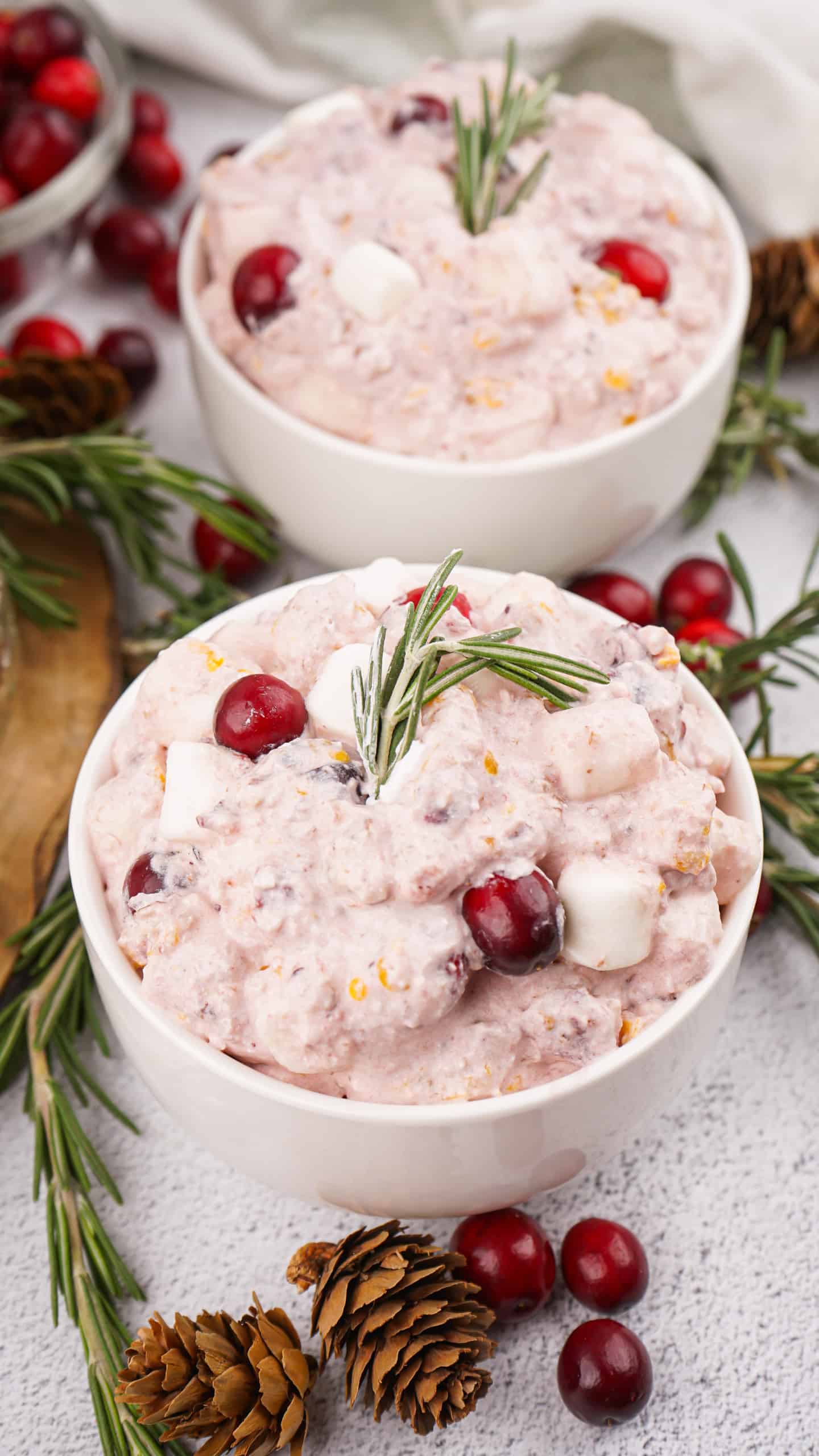 Two bowls of cranberry fluff salad with cranberries and a sprig or rosemary on top.