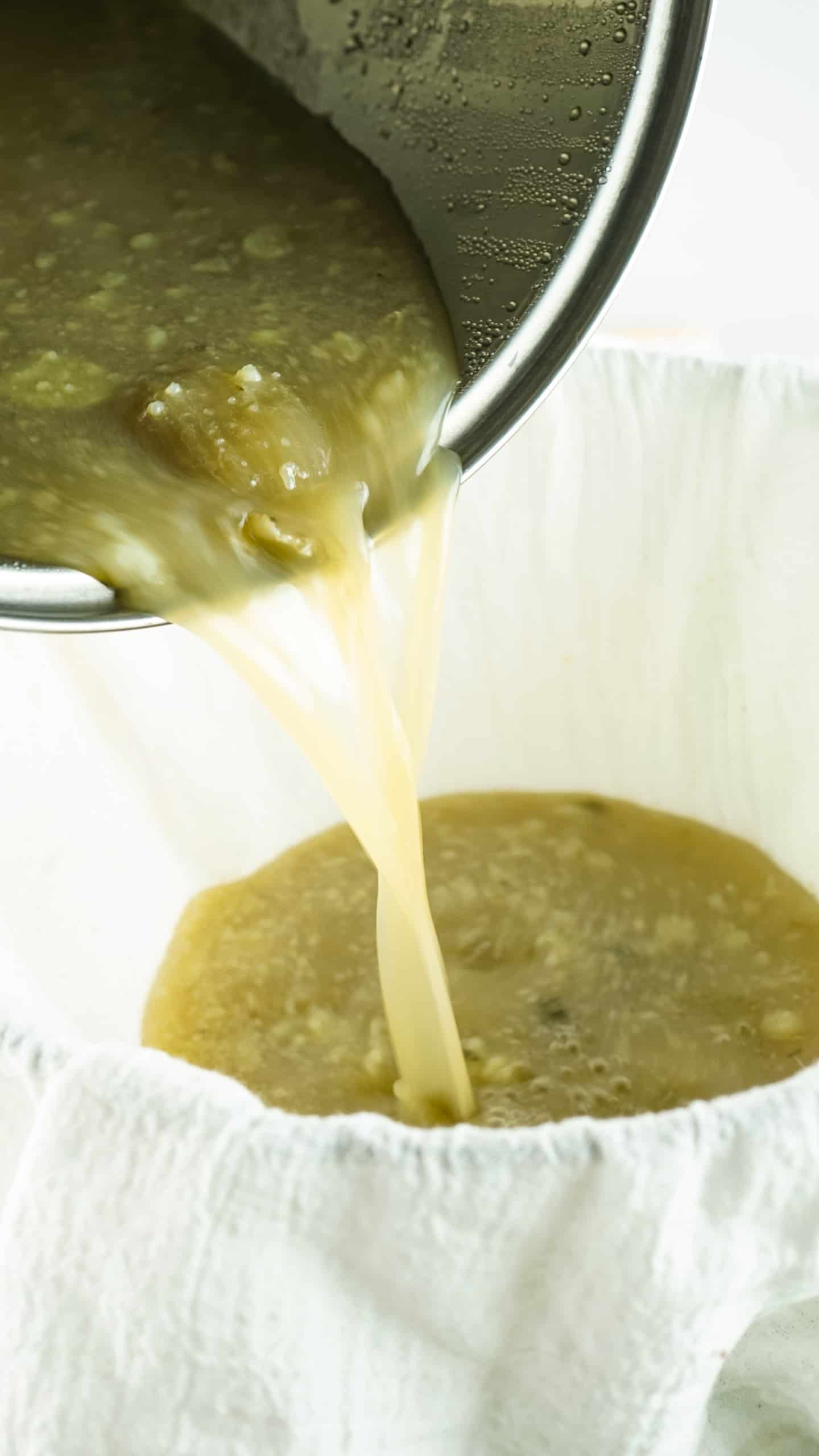 Draining solid parts out of broth through cheesecloth.