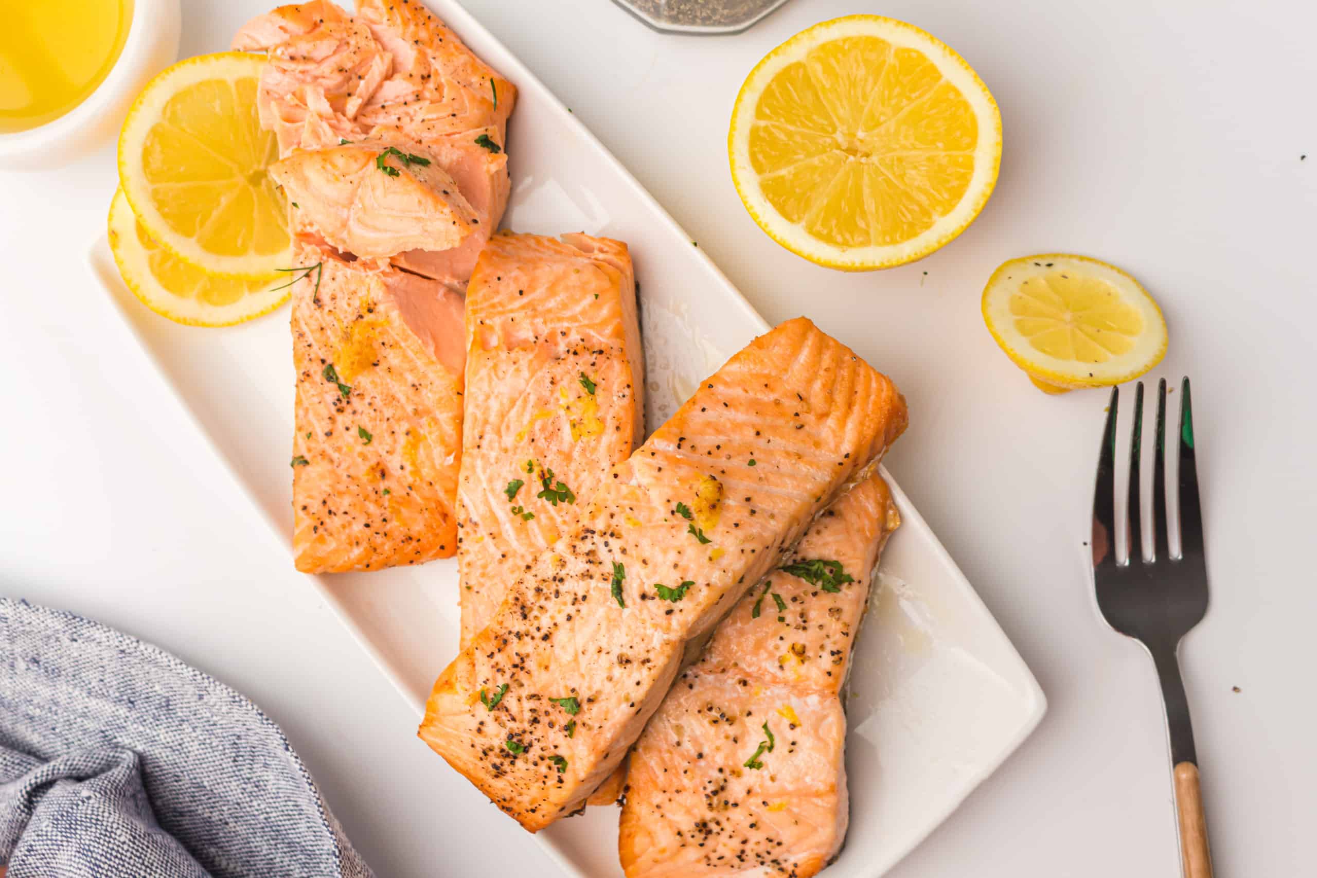 Overhead view of salmon fillets on a white rectangular plate with lemon slices on the side.