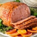 Sliced ham on a platter garnished with orange slices.