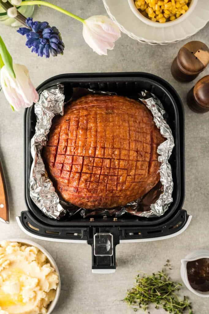 Overhead view of ham in air fryer basket lined woth foil.