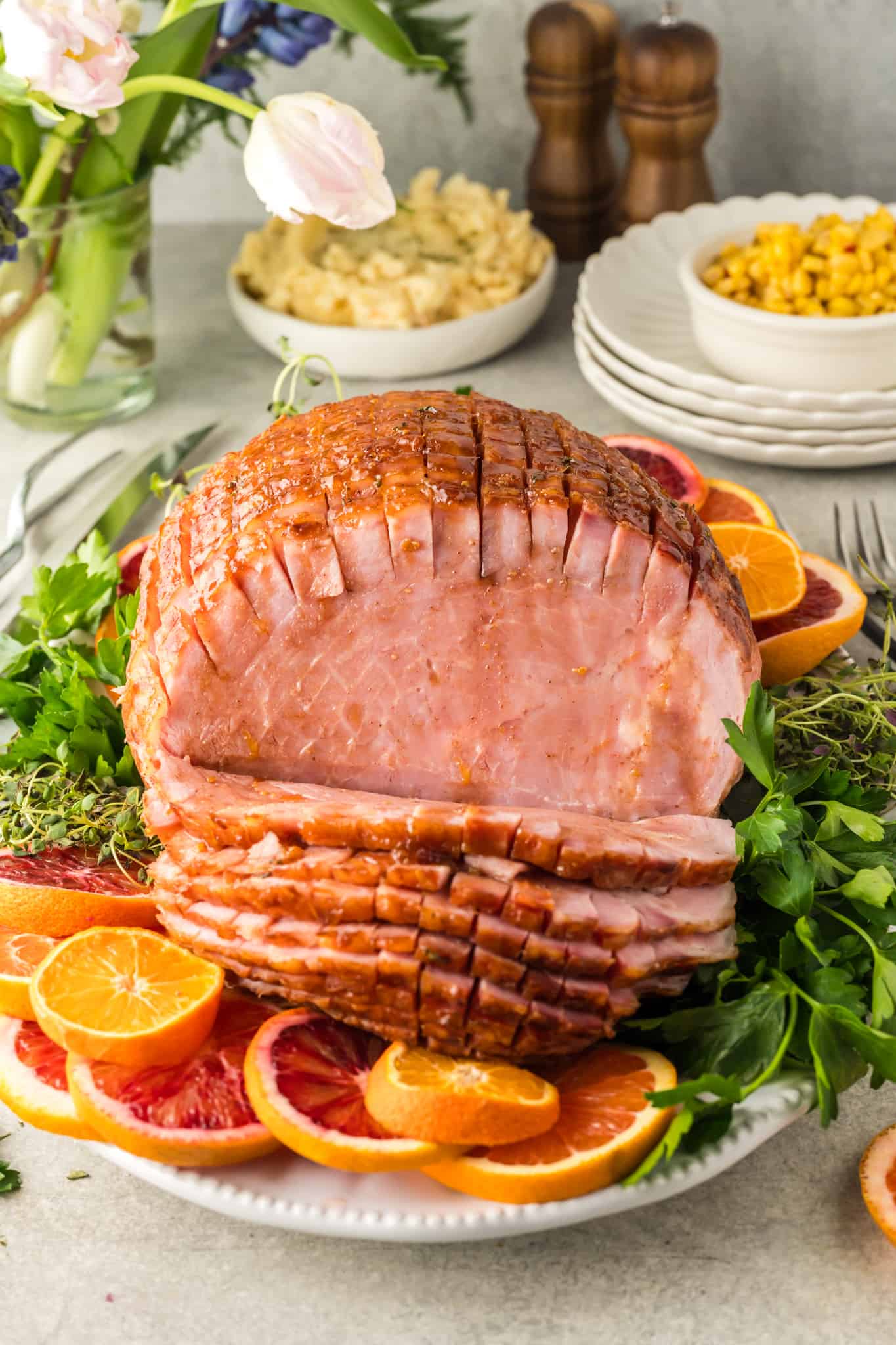 Orange-glazed ham on a plate with slices cut off and garnished with oranges.