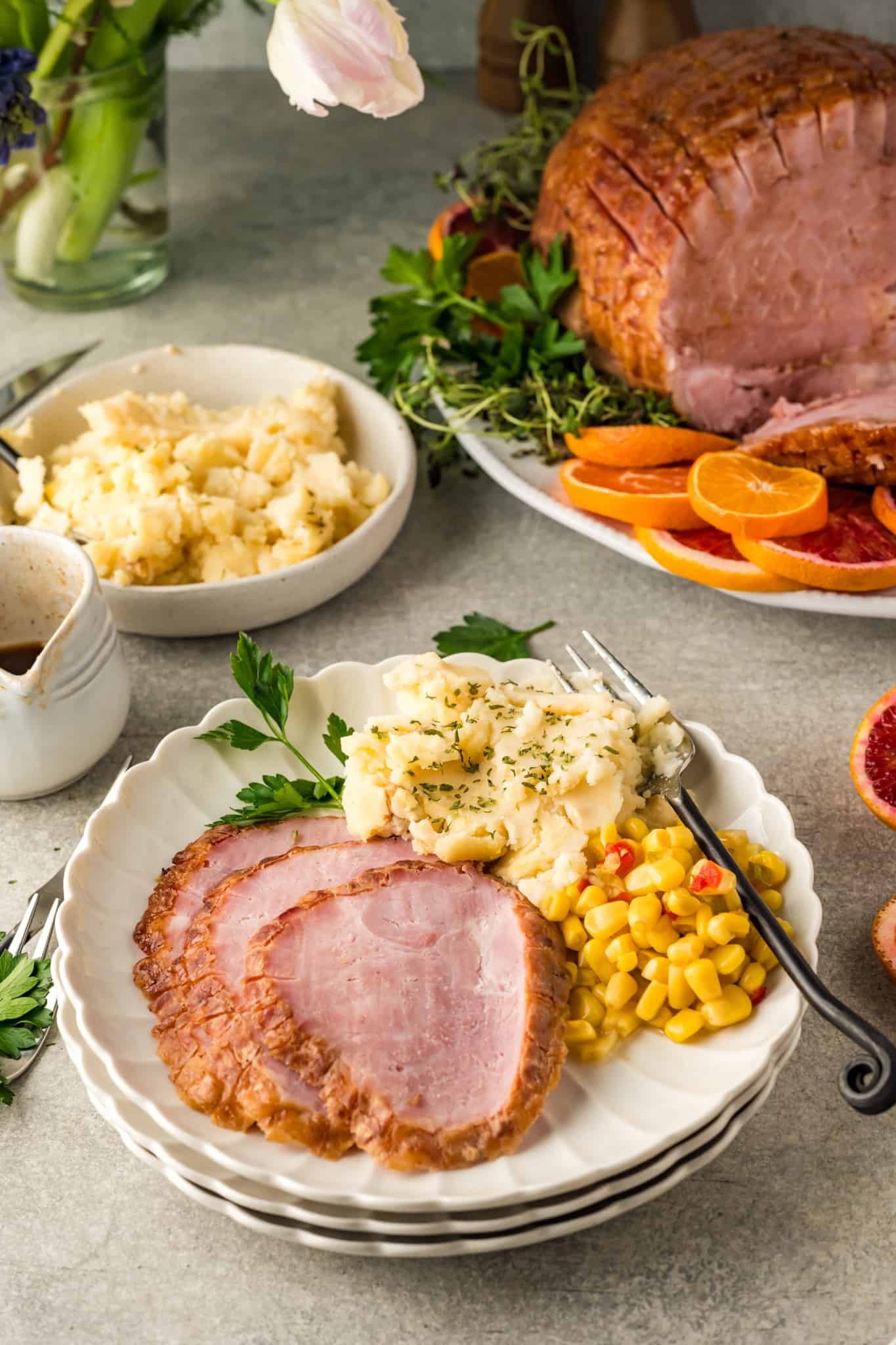 Sliced ham with mashed potatoes and corn on a white plate.