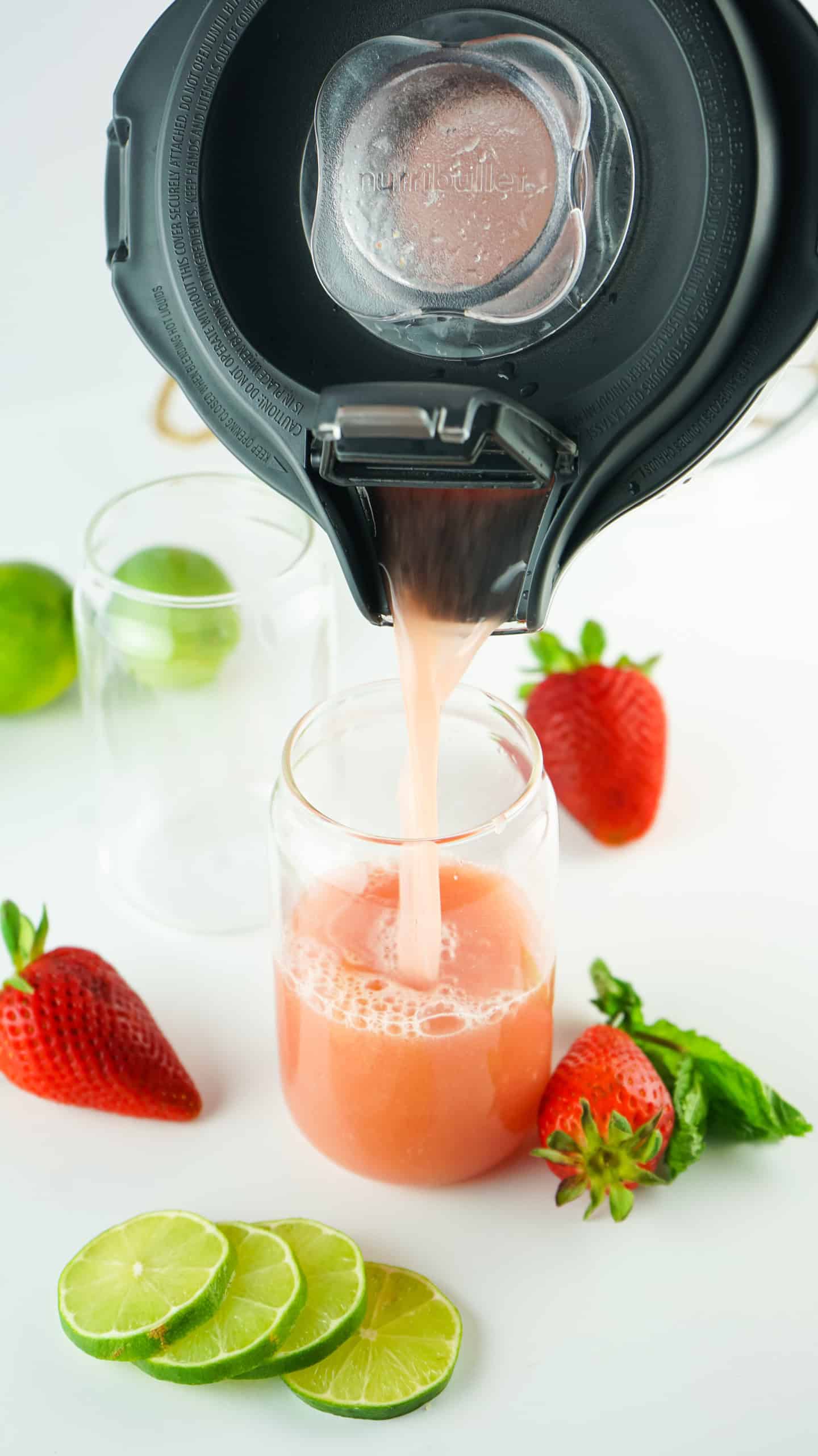 Pouring Strawberry Agua Fresca out of a blender into a glass.