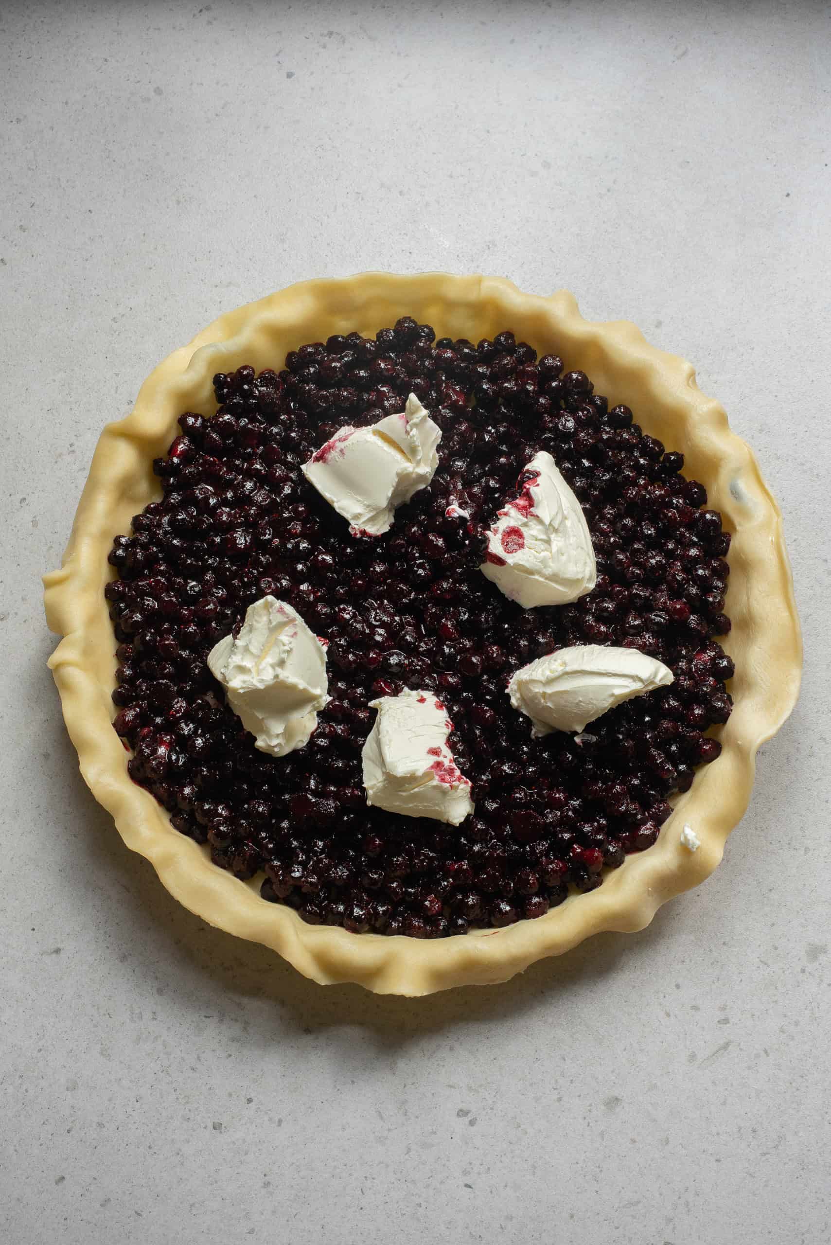 Cream cheese dollops on top of blueberries in pie crust.