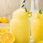 Frozen lemonade slushie in a mason jar mug with striped straws, fresh mint, and a lemon twist