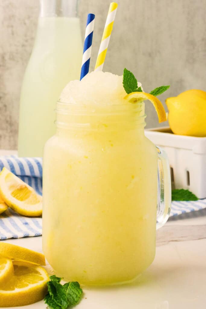 Tall mason jar of lemonade slushie garnished with mint and a curl of lemon peel