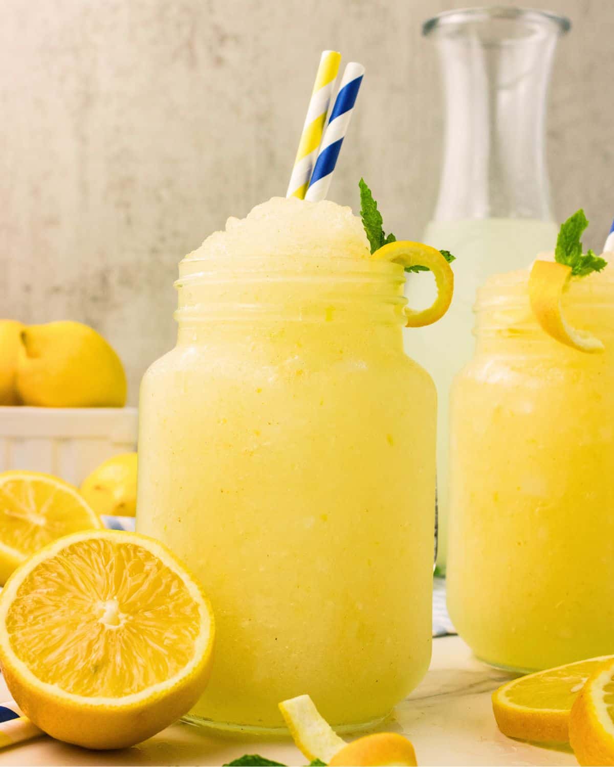 Frozen lemonade slushie in a mason jar mug with striped straws, fresh mint, and a lemon twist