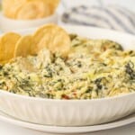 Artichoke spinach dip. in a white bowl with tortilla chip in the dip.