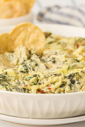 Artichoke spinach dip. in a white bowl with tortilla chip in the dip.