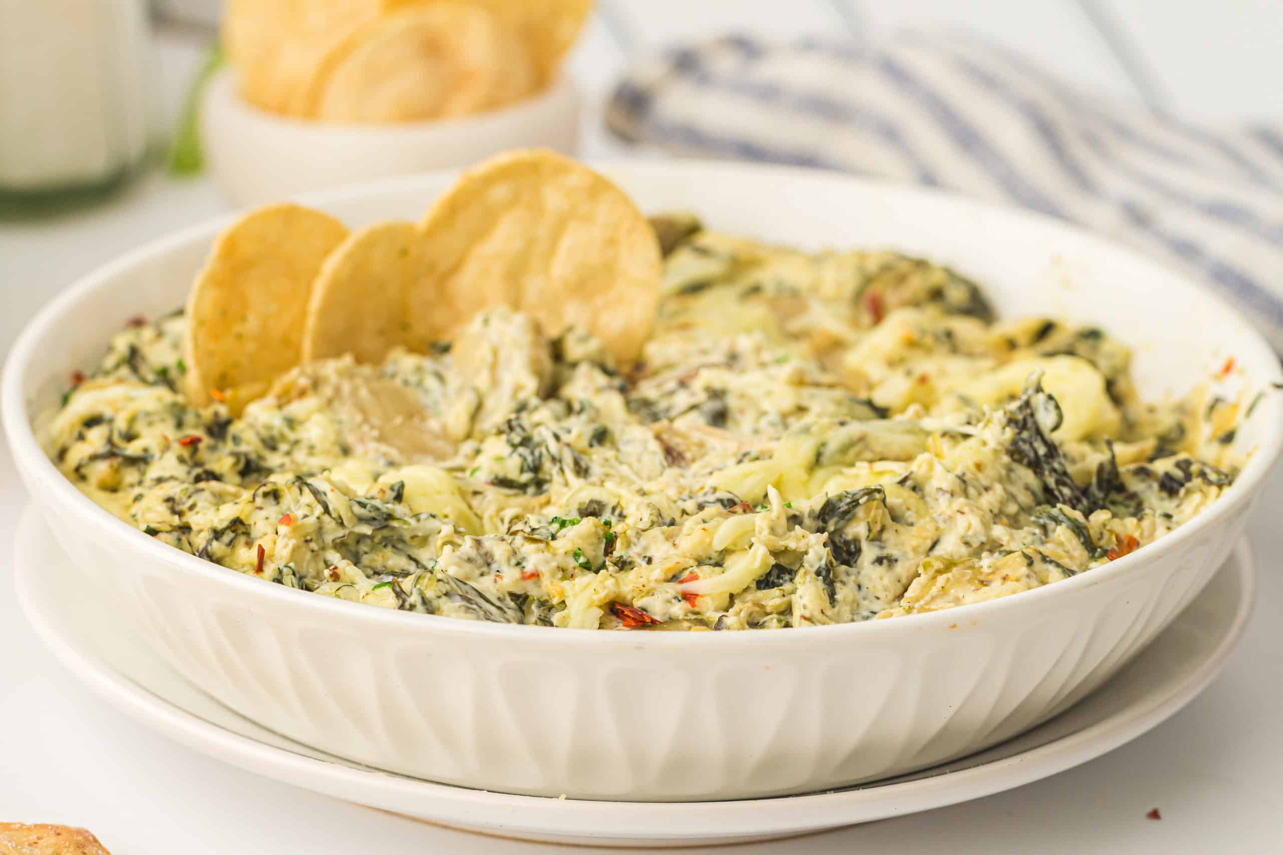Artichoke spinach dip. in a white bowl with tortilla chip in the dip.