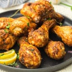 Chicken Drumsticks on a black plate with lemon wedges.