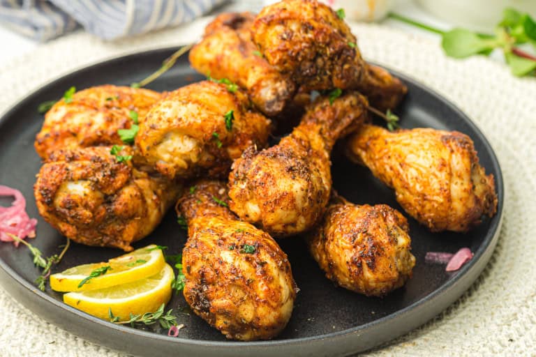 Chicken Drumsticks on a black plate with lemon wedges.