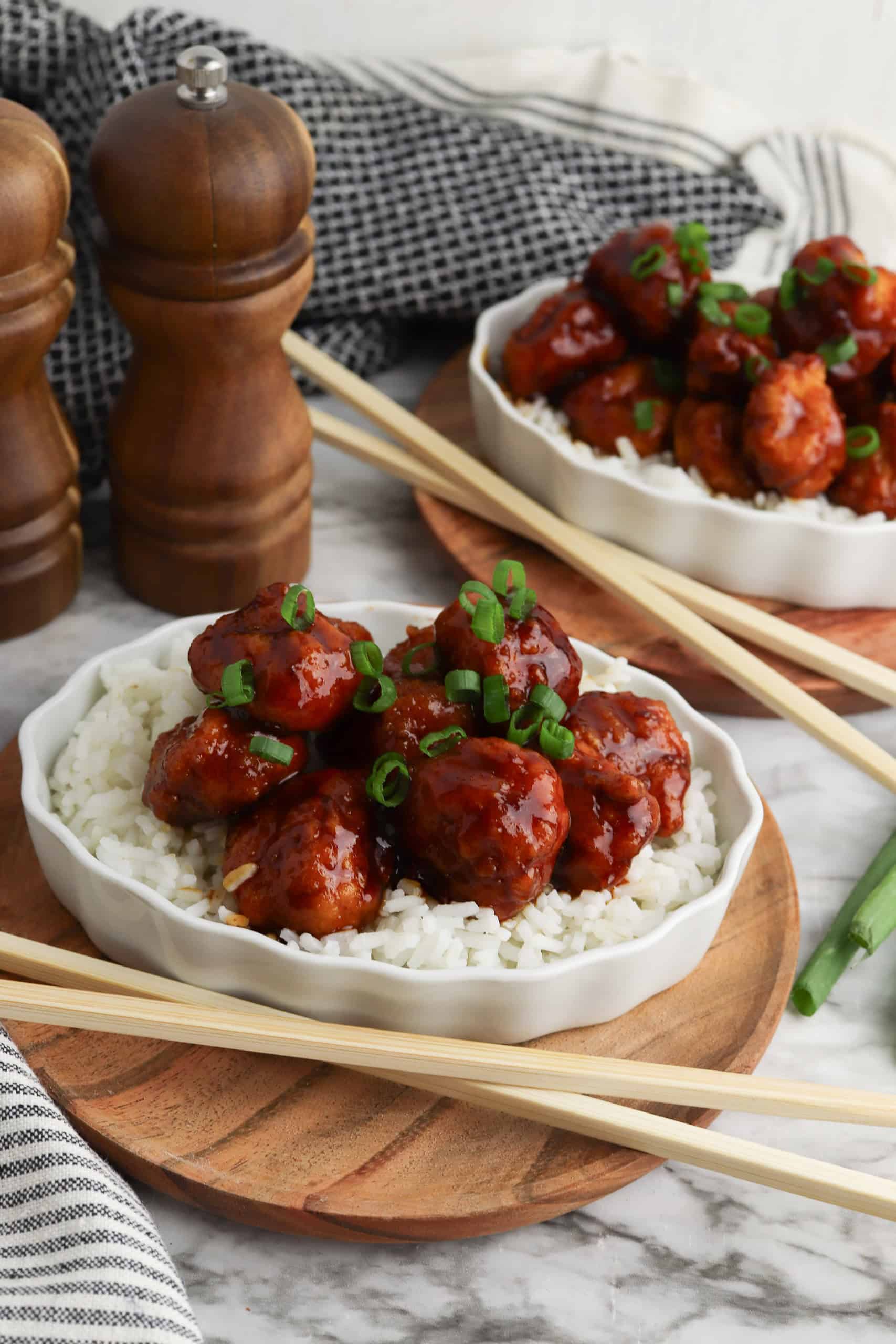 General Tsos Chicken over white rice with green onions on top and chopsticks on the side.