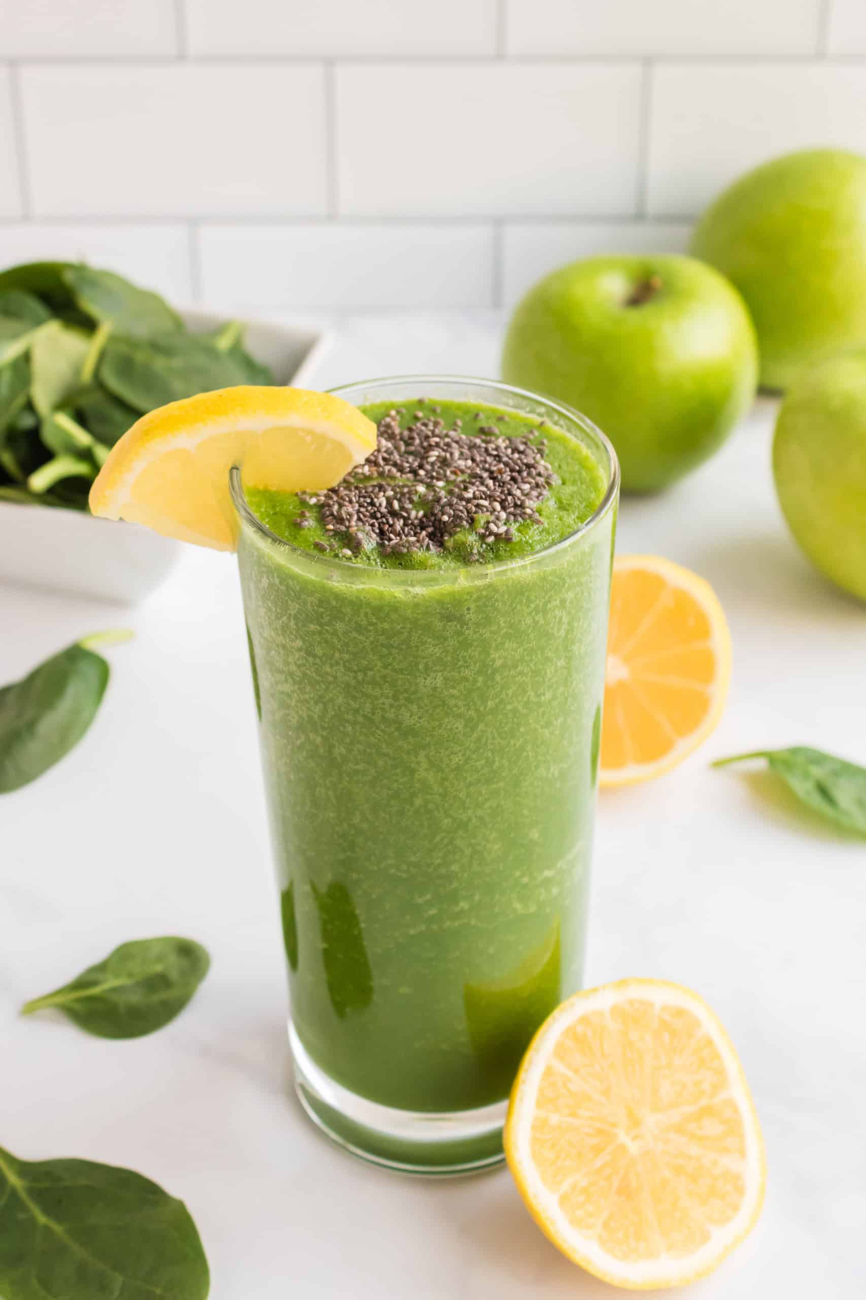 Spinach smoothie with green apples and chia seeds in a glass with a lemon slice on the side.
