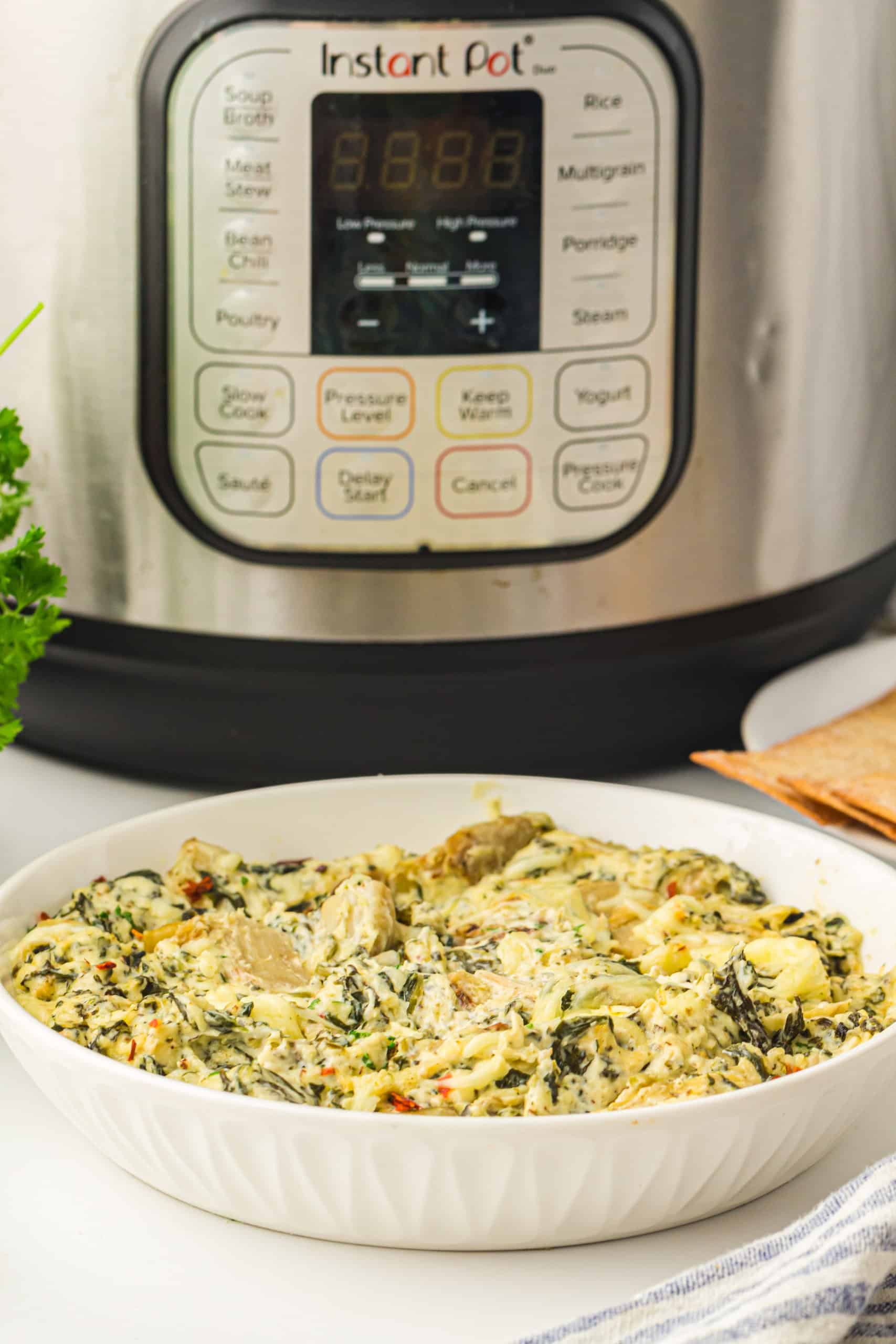 Spinach artichoke dip in a white bowl in front fo the Instant Pot.