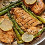 Closeup of chicken with lemon butter and asparagus in a skillet.
